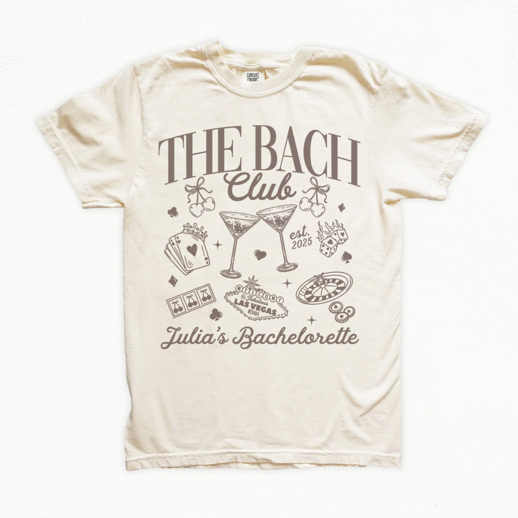 Beige bachelorette t-shirt with 'The Bach Club' and 'Julia's Bachelorette' text and graphics on a white background