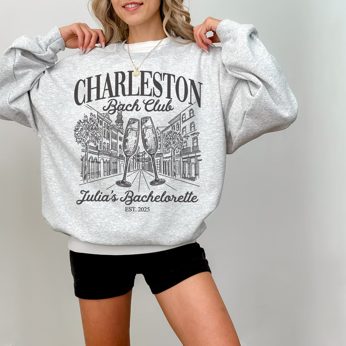 Person wearing a gray sweatshirt with 'Charleston Bachelorette' design on a plain background