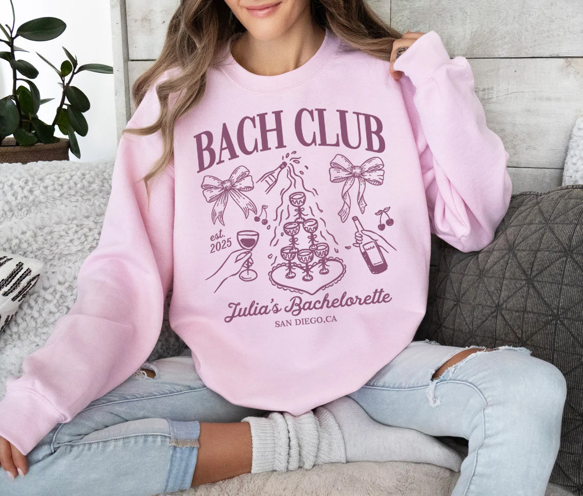 Person wearing a pink sweatshirt with 'BACH CLUB' design sitting on a couch.