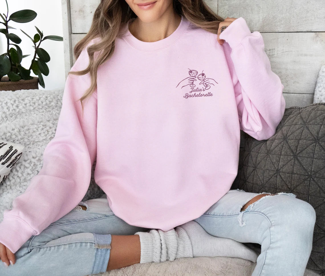 Person wearing a pink sweatshirt with a logo and text, sitting on a couch.
