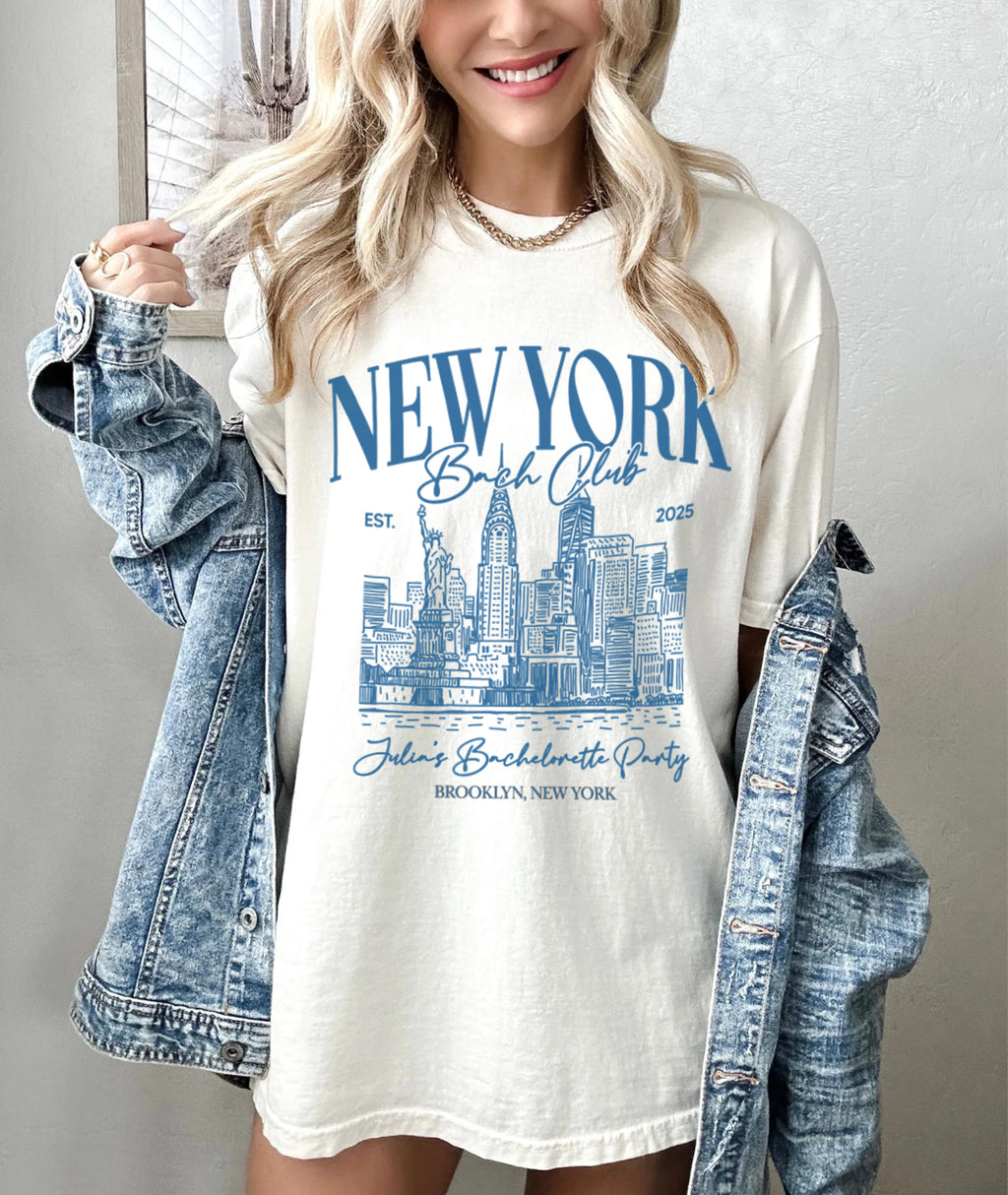 Woman wearing a white t-shirt with 'New York Bachelorette Club' design, holding a denim jacket.