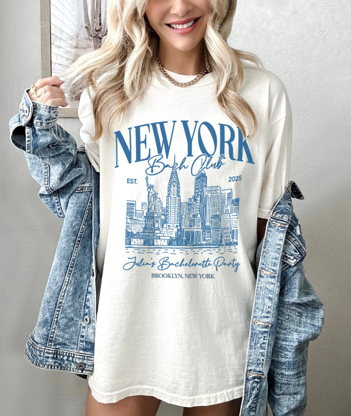 Woman wearing a white t-shirt with 'New York Bachelorette Club' design, holding a denim jacket.