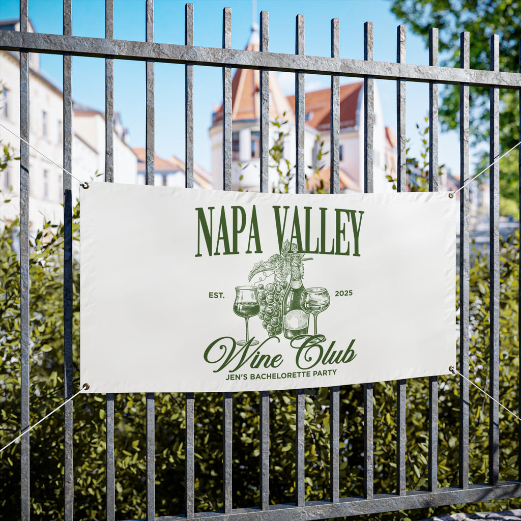 Napa Valley Wine Club sign on a metal fence with greenery and buildings in the background